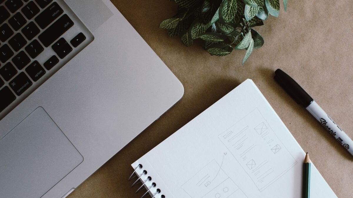 Secretária de trabalho com computador e caderno de esboços, ilustrando o planeamento de uma estratégia de branding para arquitetos.