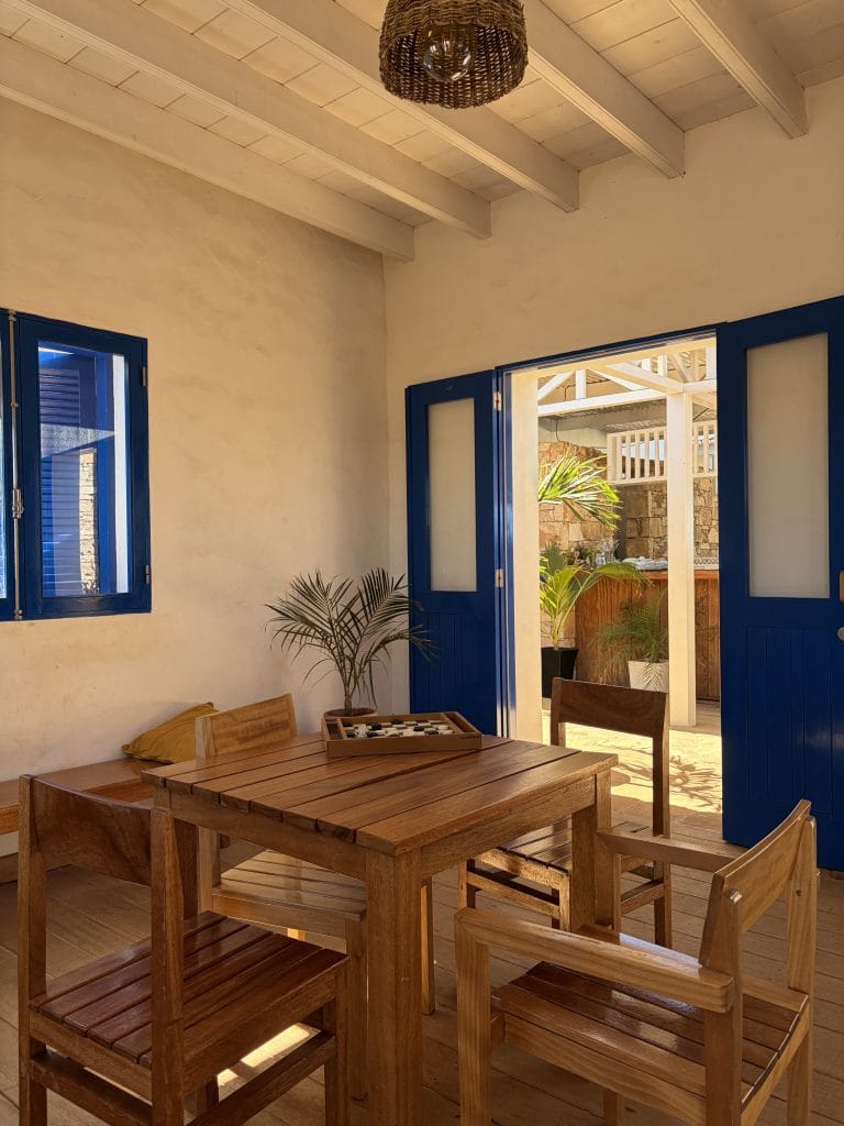 Sala de estar com mesa de madeira e portas azuis abertas para um pátio, representando uma experiência de cliente acolhedora num projeto de arquitetura.